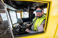 a man in a fluorescent vest drives a snow plow